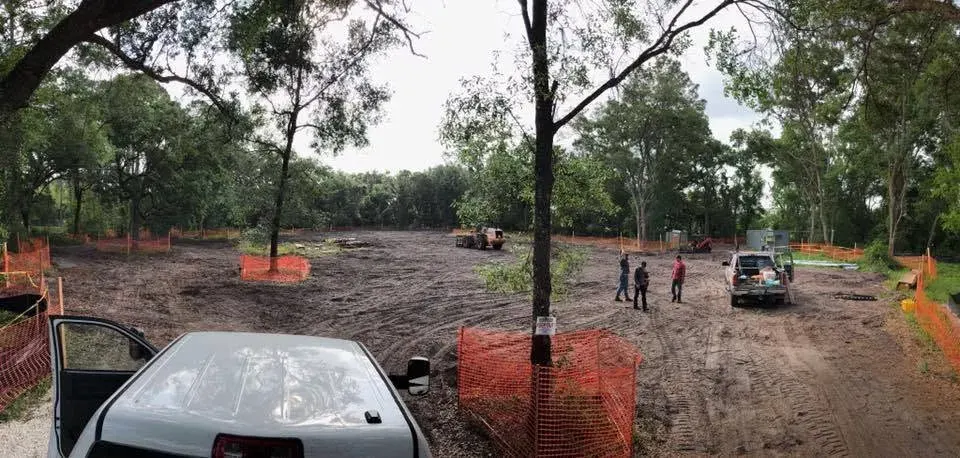 Graded lot ringed by orange tree-protection fencing with crew and loader among kept oaks near DeLand, FL